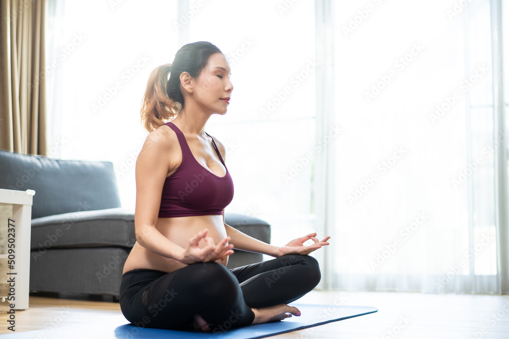 Obraz premium Asian young beautiful pregnant girl doing Yoga Pilates workout at home