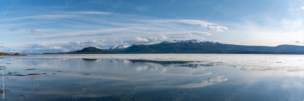 Panoramic shot of snow capped mountain view scenery seen in northern British Columbia during spring time with blue sky day and clouds.