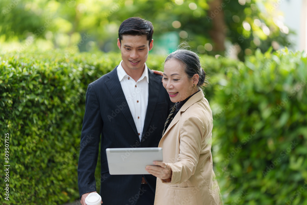 Portrait of Asian Senior Business woman and young business man discussing about project by digital tablet. Account and Finance concept. Portrait of Asian Senior Business woman and young business man discussing about project by digital tablet. Account and Finance concept.