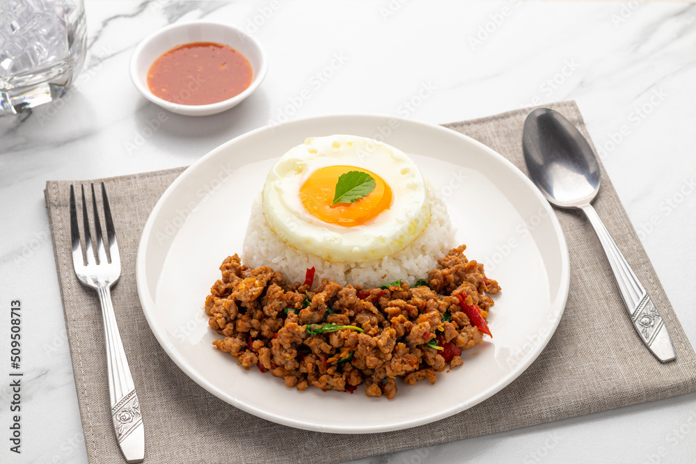 Spicy minced pork pad kra pao, minced pork stir-fried with holy basil leaves, served with plain cooked rice and a fried egg, a popular Thai single dish served from street food carts to restaurants. - obrazy, fototapety, plakaty 