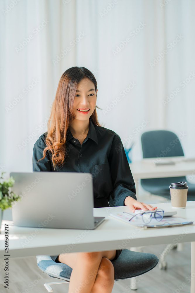 Asian businesswoman analyzing a report pointing to a graph with a pen, laptop, and calculator. In the online marketing concept of workstation accountant's vertical e-commerce landscape Asian businesswoman analyzing a report pointing to a graph with a pen, laptop, and calculator. In the online marketing concept of workstation accountant's vertical e-commerce landscape