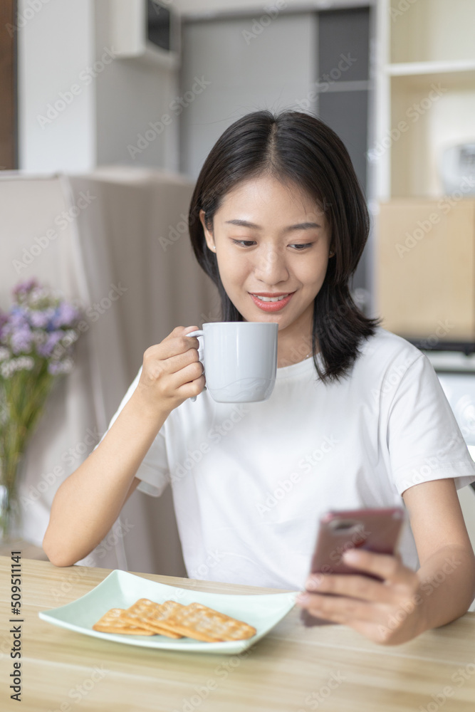 Asian woman eats breakfast with crackers (Healthy whole grain) and juice, Use your phone or mobile phone to search for morning news, Small room in condominium background, Wake-up activities. Asian woman eats breakfast with crackers (Healthy whole grain) and juice, Use your phone or mobile phone to search for morning news, Small room in condominium background, Wake-up activities.