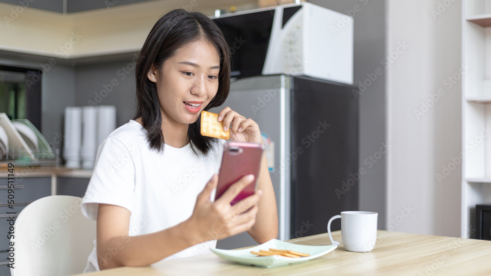 Asian woman eats breakfast with crackers (Healthy whole grain) and juice, Use your phone or mobile phone to search for morning news, Small room in condominium background, Wake-up activities. Asian woman eats breakfast with crackers (Healthy whole grain) and juice, Use your phone or mobile phone to search for morning news, Small room in condominium background, Wake-up activities.