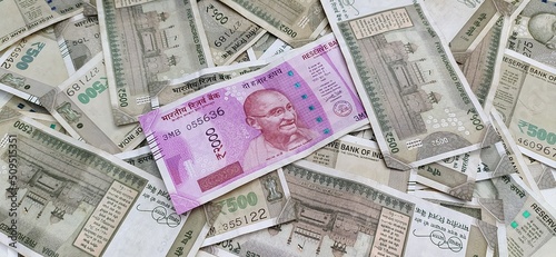 Single pink coloured two thousand indian currency bank note with mahatma ghandhi face isolated on bunch of scattered five hundred rupee notes. Closeup macro top view. Wealth savings concept background