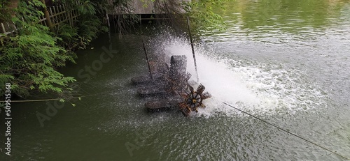 Working old vintage traditional electric power rotating water wheel in river stream or pond to increase oxigen level inside water and increasing flow. Beautiful horizontal close up side view. photo