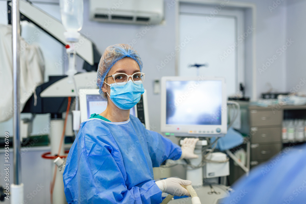 Anesthetist Working In Operating Theatre Wearing Protecive Gear checking monitors while sedating patient before surgical procedure in hospital Anesthetist Working In Operating Theatre Wearing Protecive Gear checking monitors while sedating patient before surgical procedure in hospital