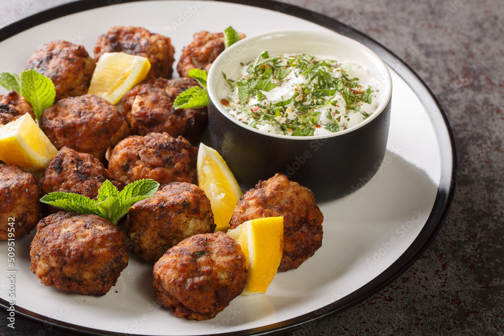 Juicy Baked Greek Meatballs Keftedakia with tzatziki sauce and lemon on a white plate on a table. Horizontal