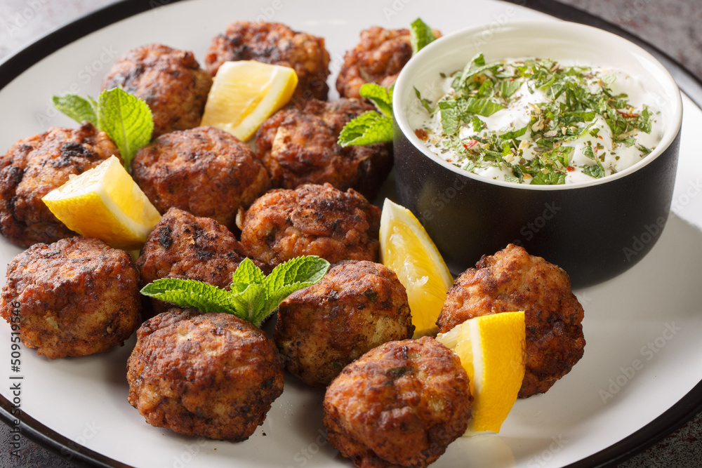 Fried Keftedakia greek veal meatballs served with tzatziki sauce and lemon on a white plate on a table. Horizontal