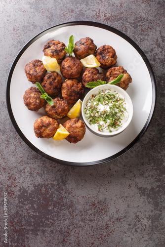 Keftedakia fried greek meatballs with tzatziki sauce and lemon on a white plate on a table. Vertical top view from above photo