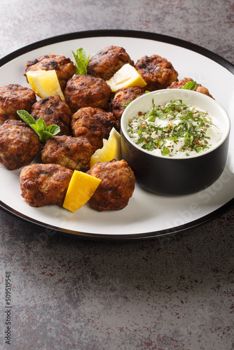Keftedakia fried greek meatballs with tzatziki sauce and lemon on a white plate on a table. Vertical