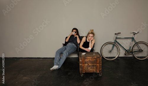 Fotografie Two exhausted young women  with hangover after a party sit in chairs in studio i