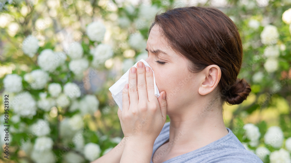 Middle-aged woman blowing her nose in a flowering garden. Middle-aged woman blowing her nose in a flowering garden.