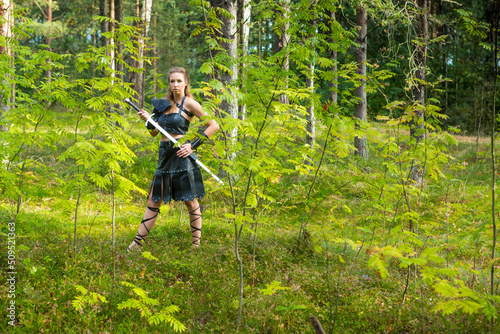 long-haired female warrior wearing leather skirt, bracer, lorica and rerebrace with sharp estramacon in her hand stands in the fall forest photo