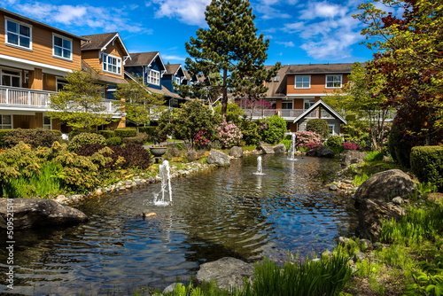 Residential district with village of townhouses  in a picturesque location near a pond with a fountain in the city of Richmond © Alex Lyubar