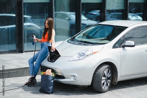 Eco electric car concept. Woman waiting electric car to charge. © Serhii