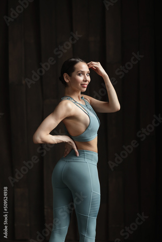 Fitness woman with perfect athletic body in sportswear, back view. Young slim girl posing in the studio, wooden wall