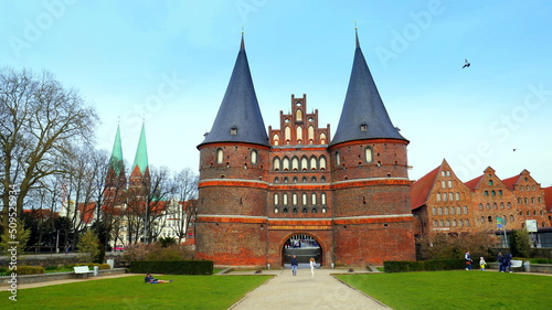Lübeck Holstentor mit zwei Spitztürmen neben Salzspeichern und Grünanlage unter blauem Himmel