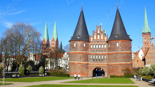 Lübeck Holstentor mit Spitztürmen und Kirchtürmen in Grünanlage unter blauem Himmel