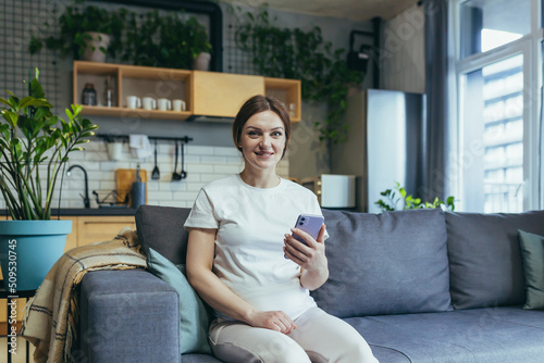 Happy pregnant woman at home rejoices with phone smiling at home and looking at camera