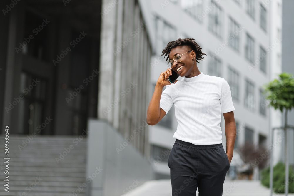 Side view portrait of smiling young african american woman walking and talking with mobile phone outside. Close up portrait of attractive young woman smiling and talking on smartphone. Side view portrait of smiling young african american woman walking and talking with mobile phone outside. Close up portrait of attractive young woman smiling and talking on smartphone.