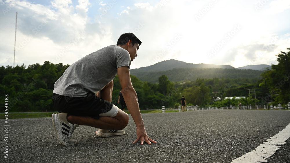 Fototapeta premium Young sportsman in starting position, ready to run outdoors in the morning. Health and sport concept