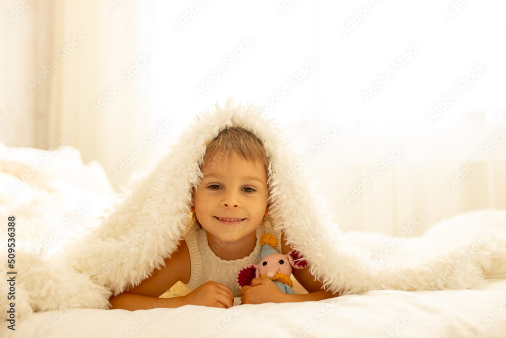 Obraz premium Little toddler child, cute kid with knitted small cute animal toy, lying in bed