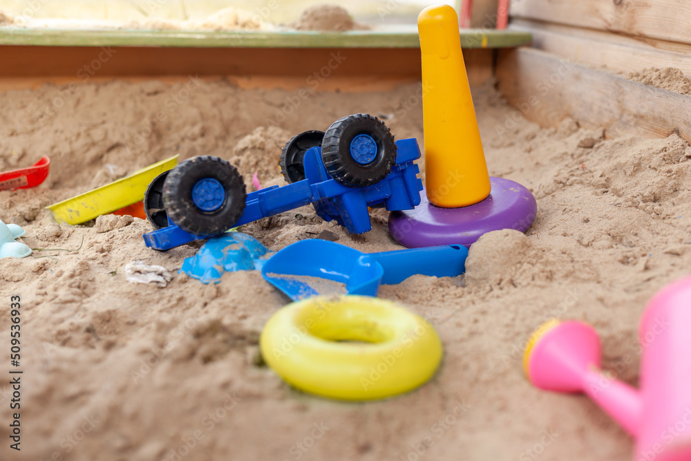 Sandbox outdoor. Children's wooden sandbox with various toys for the game. Summer concept. Colored toys and cars on the children's sandbox. Selective focus with shallow depth of field
