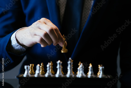 Unrecognizable male in suit holding golden king while playing chess against gray background