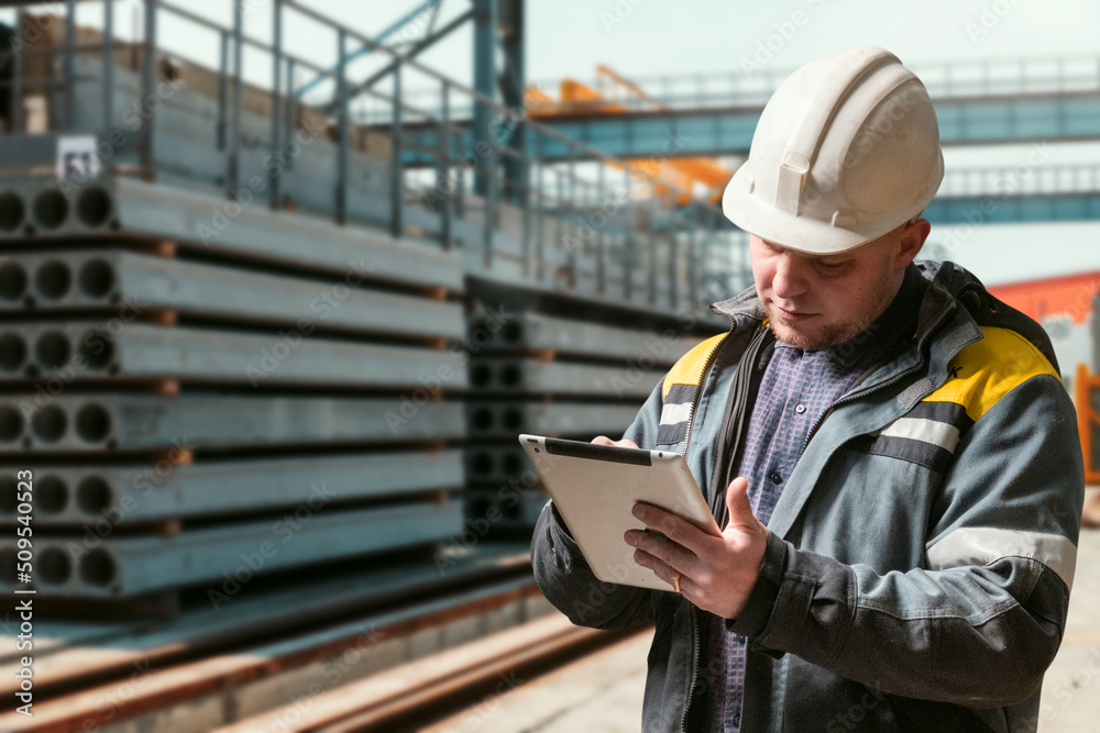 civil engineer with a tablet in his hands stands in the warehouse of finished products of a factory for the production of reinforced concrete products civil engineer with a tablet in his hands stands in the warehouse of finished products of a factory for the production of reinforced concrete products
