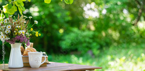 Fototapeta Naklejka Na Ścianę i Meble -  Bouquet of meadow flowers, croissant, cup of tea or coffee, books on table in summer garden. Rest in garden, reading books, breakfast, vacations in nature concept. Summertime in garden on backyard