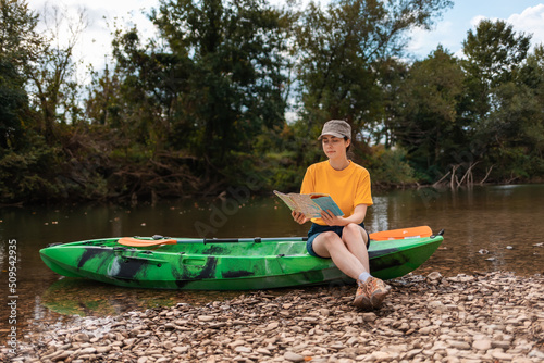 Pretty caucasian young woman is sitting on a kayak, holding a paper map. Copy space. The concept of the World Tourism Day