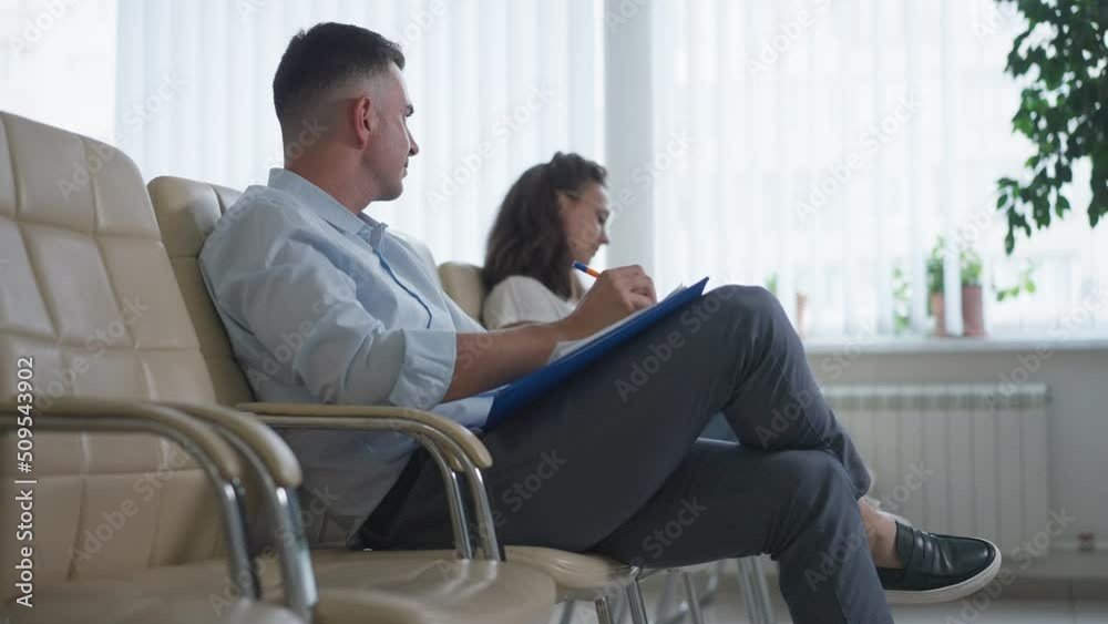 Side view concentrated man sitting with annoying woman in comfortable conference room writing in slow motion shaking head. Caucasian managers learning business innovations in office Side view concentrated man sitting with annoying woman in comfortable conference room writing in slow motion shaking head. Caucasian managers learning business innovations in office