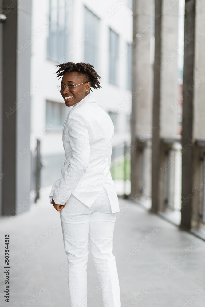 Close up shot of beautiful stylish African woman in modern city, wearing wearing white elegant suit with eyelgasses, looking at camera. Fashion photo, copy space. Close up shot of beautiful stylish African woman in modern city, wearing wearing white elegant suit with eyelgasses, looking at camera. Fashion photo, copy space.