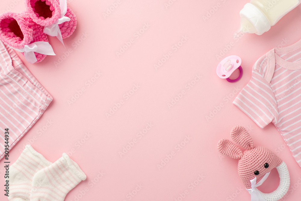 Baby accessories concept. Top view photo of pink infant clothes shirt shorts socks booties baby's dummy bottle and knitted bunny rattle toy on isolated pastel pink background with copyspace