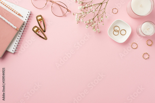 Business concept. Top view photo of workplace candles diaries pencils stylish glasses gold rings barrettes and white gypsophila flowers on isolated pastel pink background with empty space
