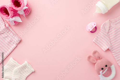 Baby accessories concept. Top view photo of pink infant clothes shirt shorts socks booties baby's dummy bottle and knitted bunny rattle toy on isolated pastel pink background with copyspace © ActionGP