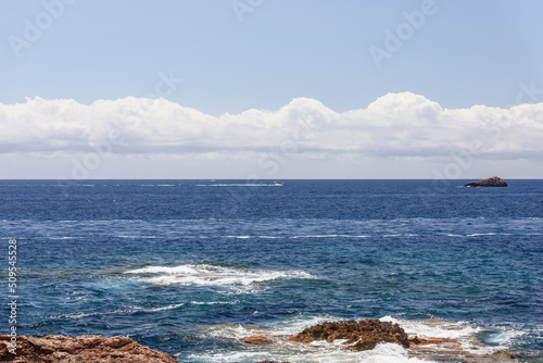 Small waves on sea surface and small white motorboat crosses the bay in distance, Ibiza, Balearic Islands, Spain