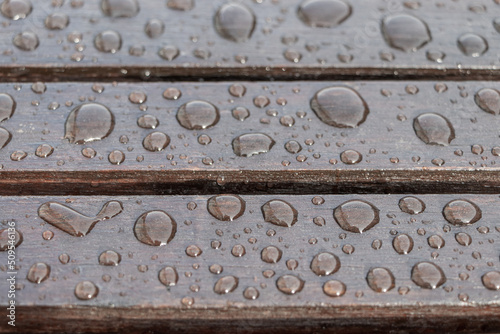 Wooden planks covered by water drops, background for rainy weather. Wet brown boards close up. Selective focus
