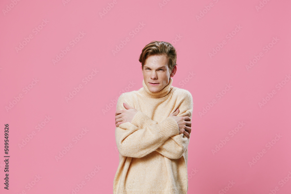 a frozen guy in a long beige sweater stands on a pink background and warms himself by rubbing himself with his hands a frozen guy in a long beige sweater stands on a pink background and warms himself by rubbing himself with his hands