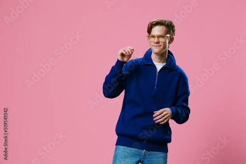 handsome, happy guy in a blue sweater and stylish glasses enjoys life standing on a pink background