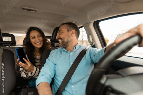 Couple Using Car Navigation App On Smartphone Sitting In Automobile