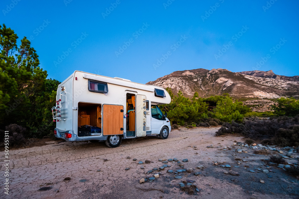 Motorhome RV parked on the beach under a tree next to main road, Crete, Greece.