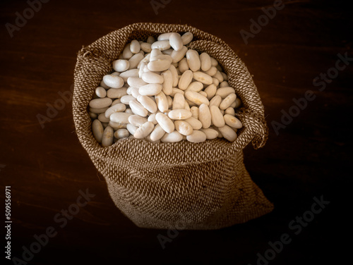 Dried white beans in a sack against a dark background