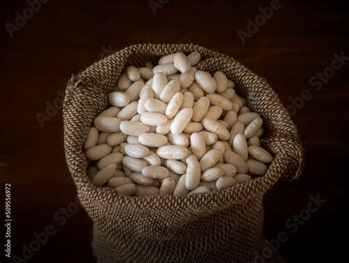 Dried white beans in a sack against a dark background