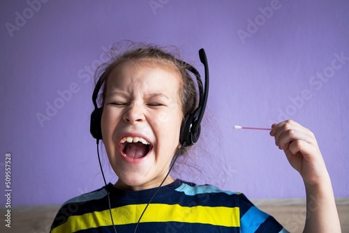 the girl listens to music in big headphones and through the pain cleans her ears with ear sticks from loud songs