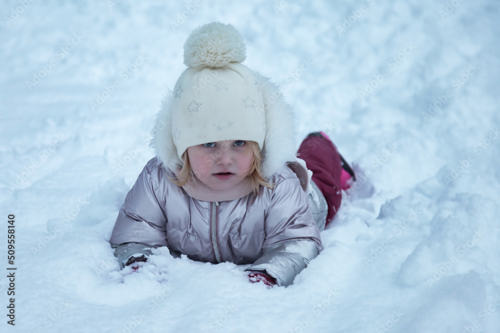 Winter portrait happy little girl in snowy public park in warm clothes