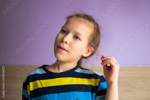 girl child in a striped turtleneck shows joy and happiness because of a cotton stick in the ear, where it became mirror-clear