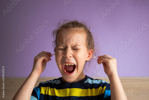 girl child in a striped turtleneck shows pain due to a cotton stick in the ear, where it is very dirty