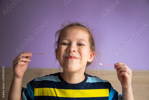 girl child in a striped turtleneck shows joy and happiness because of a cotton stick in the ear, where it became mirror-clear
