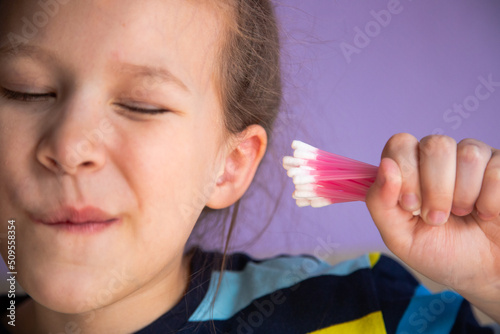 a child girl in a striped turtleneck puts a lot of cotton sticks in her ear, not much dirt will fit